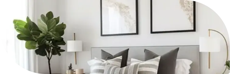 "Minimalist bedroom with a neatly made bed, framed artwork, bedside tables with lamps, and a large green plant